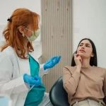 Dentist in a mask and blue gloves talking with a thoughtful patient seated in a dental chair